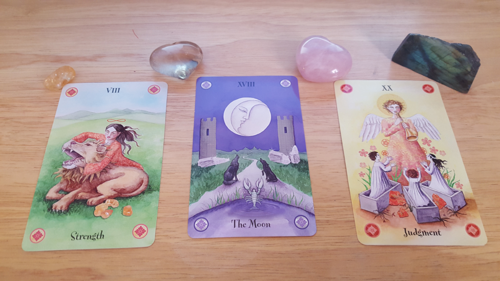 three tarot cards on a tan table with three crystals above each one